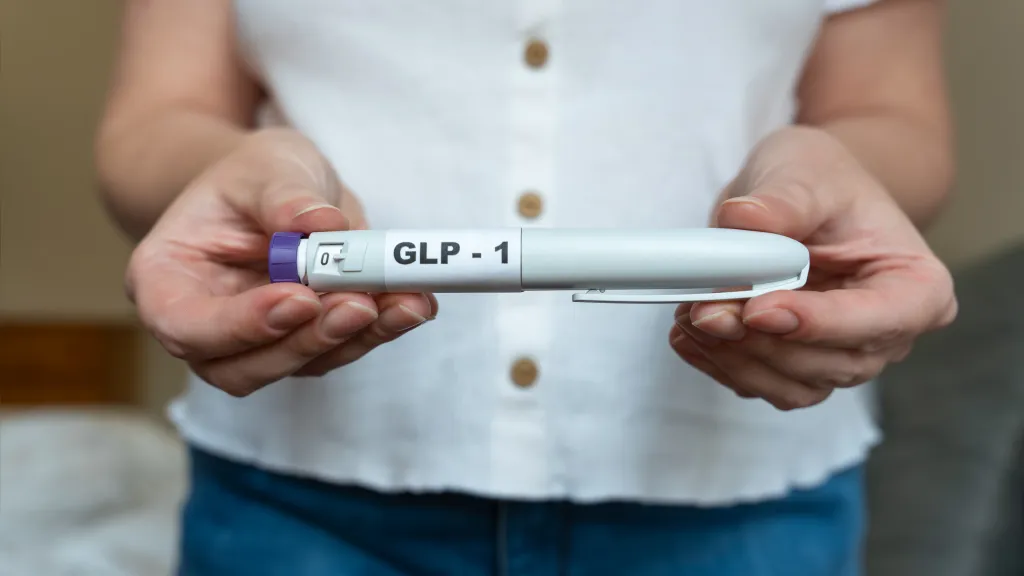 A woman holds a GLP-1 injection pen in front of her abdomen for weight management.