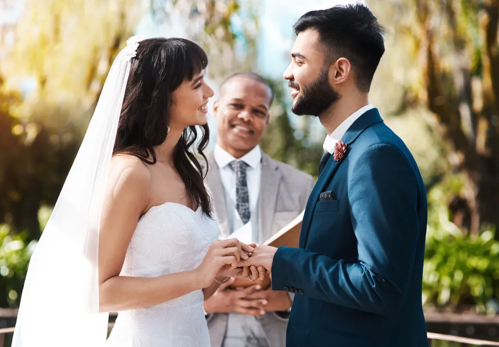 A bride and groom exchange vows while holding hands during their wedding ceremony with an officiant in the background.
