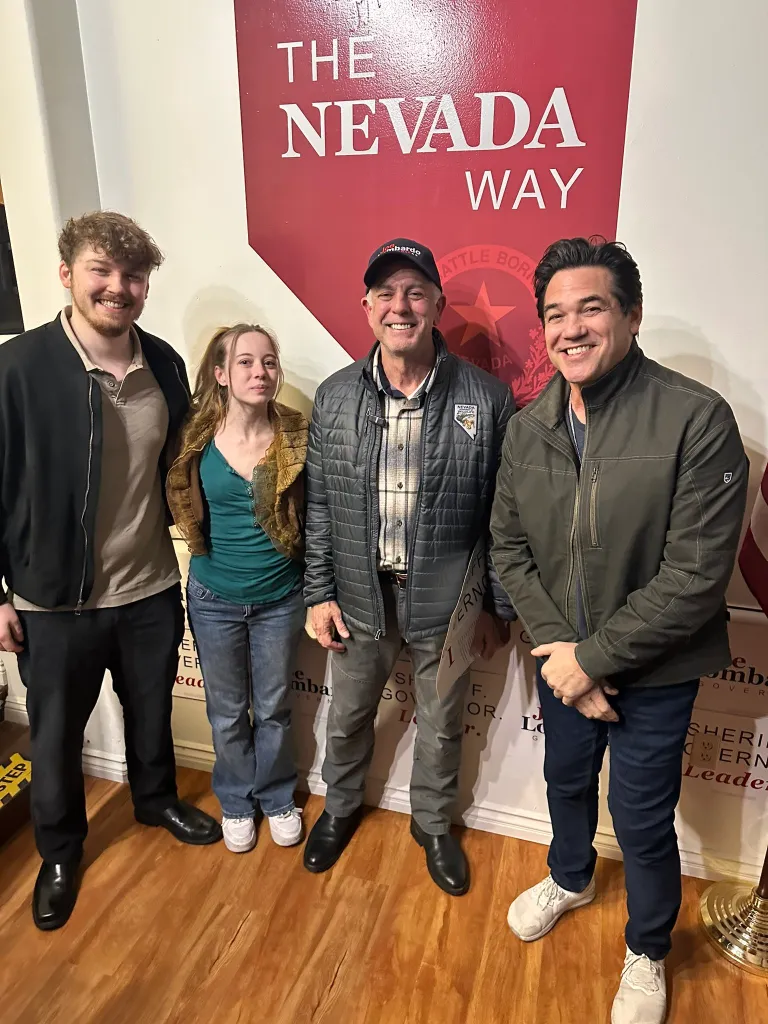 Dean Cain Lombardo standing with three other people in front of a sign that reads