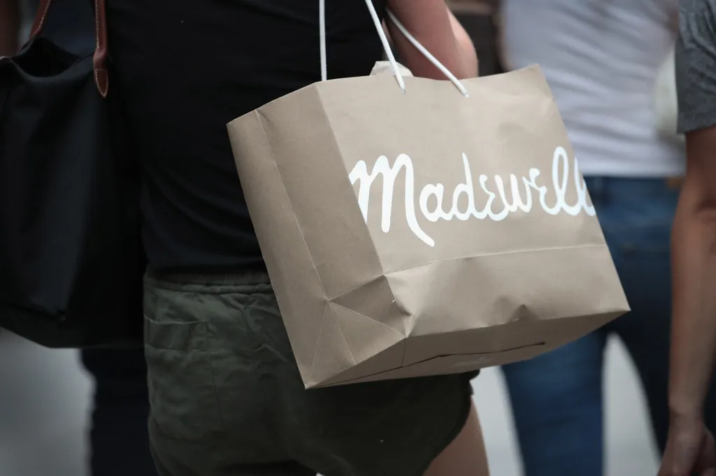 A person carrying a brown Madewell shopping bag.