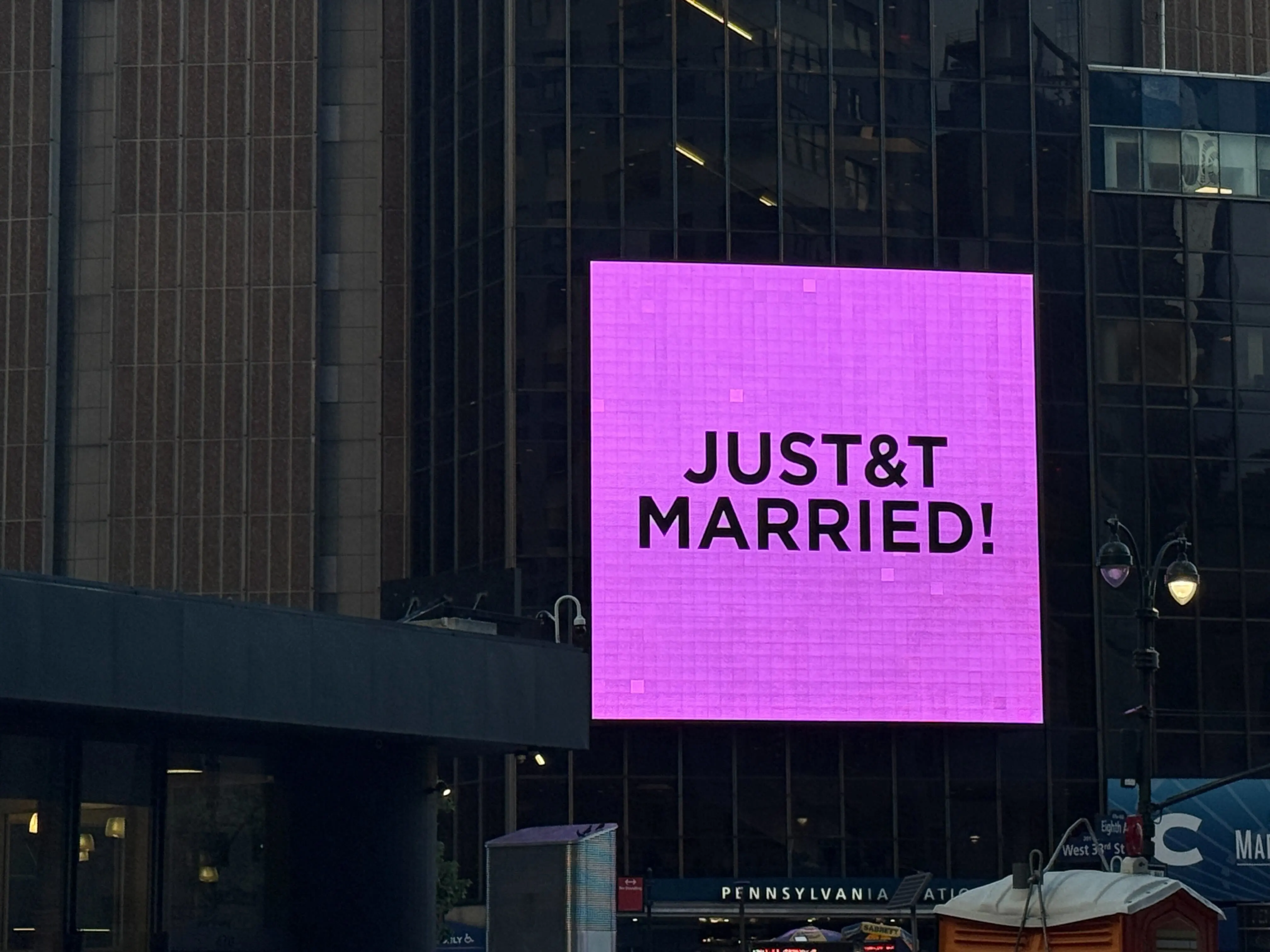 A bright pink digital billboard on a city building reads