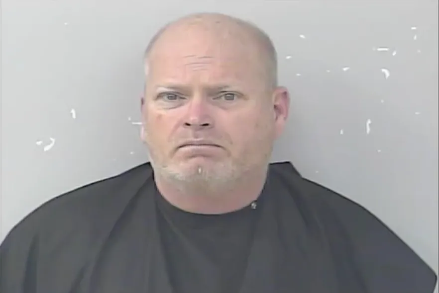 Mugshot of a balding white man with a gray goatee, wearing a dark shirt.
