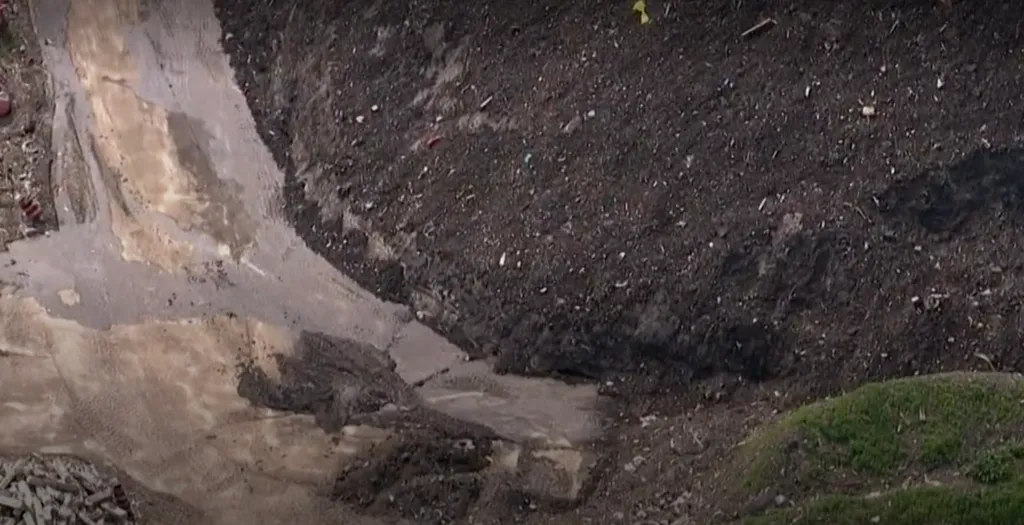 Close-up aerial view of a large sinkhole with broken concrete and debris.