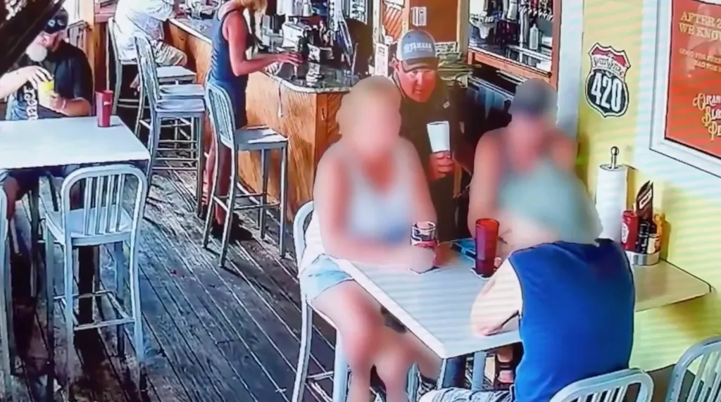 Several people, some blurred, at tables and a bar in a restaurant or bar setting.