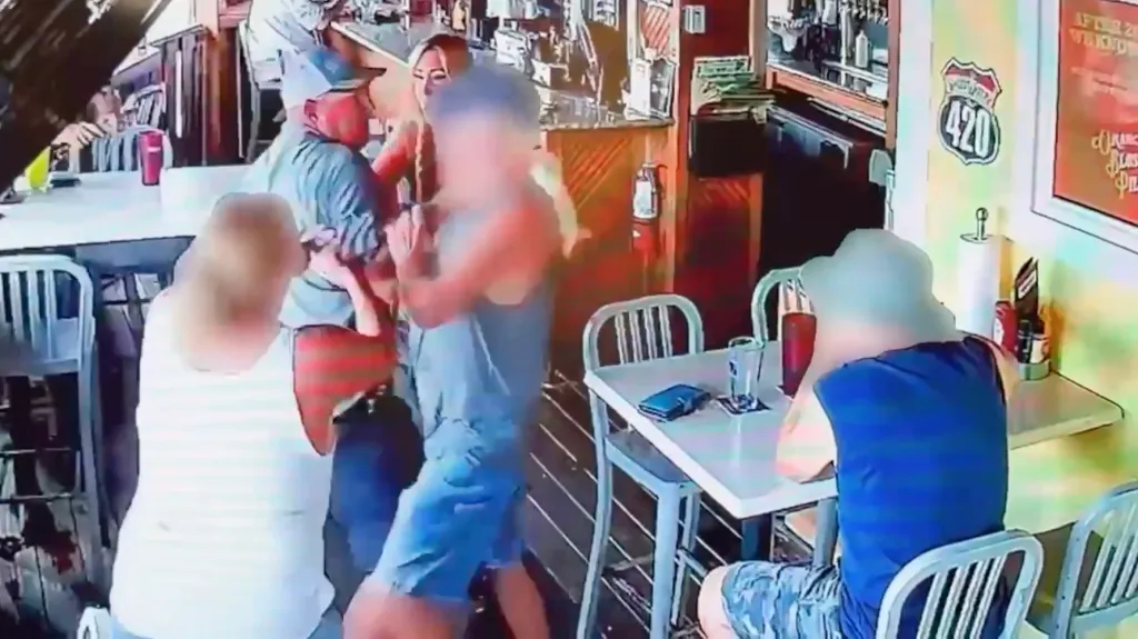 A man in a blue shirt attempts to punch another man in a tank top at a bar.
