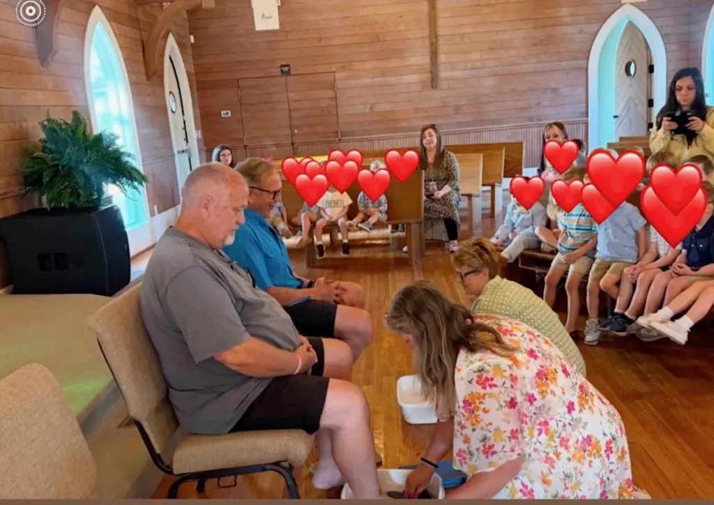 A woman washes the feet of a man in a church, while other people sit in pews.