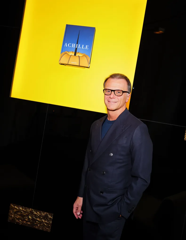 Achille Salvagni standing by a bright yellow wall with his book 