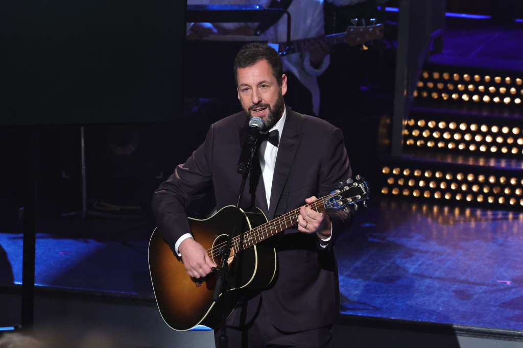 Adam Sandler performing with a guitar and microphone during the 