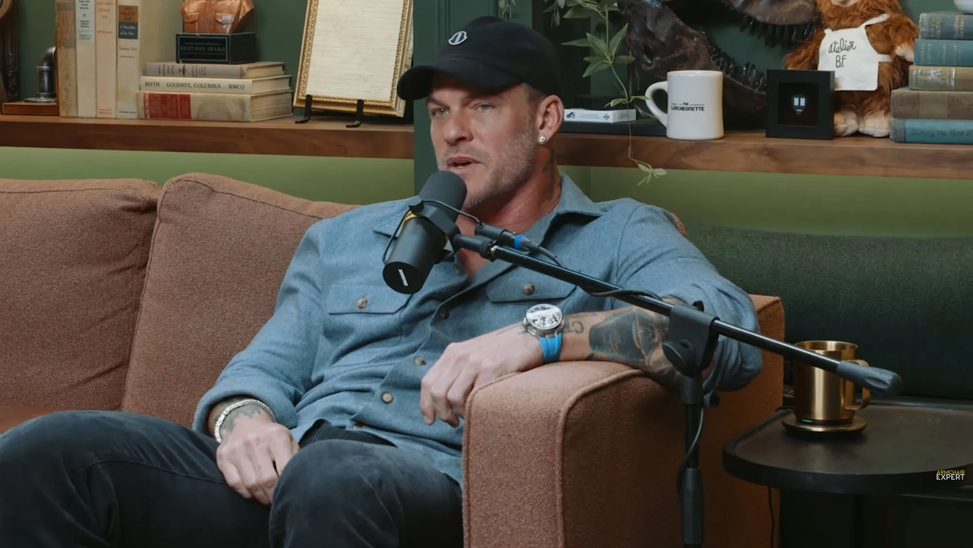 Alan Ritchson speaking into a microphone on a couch.
