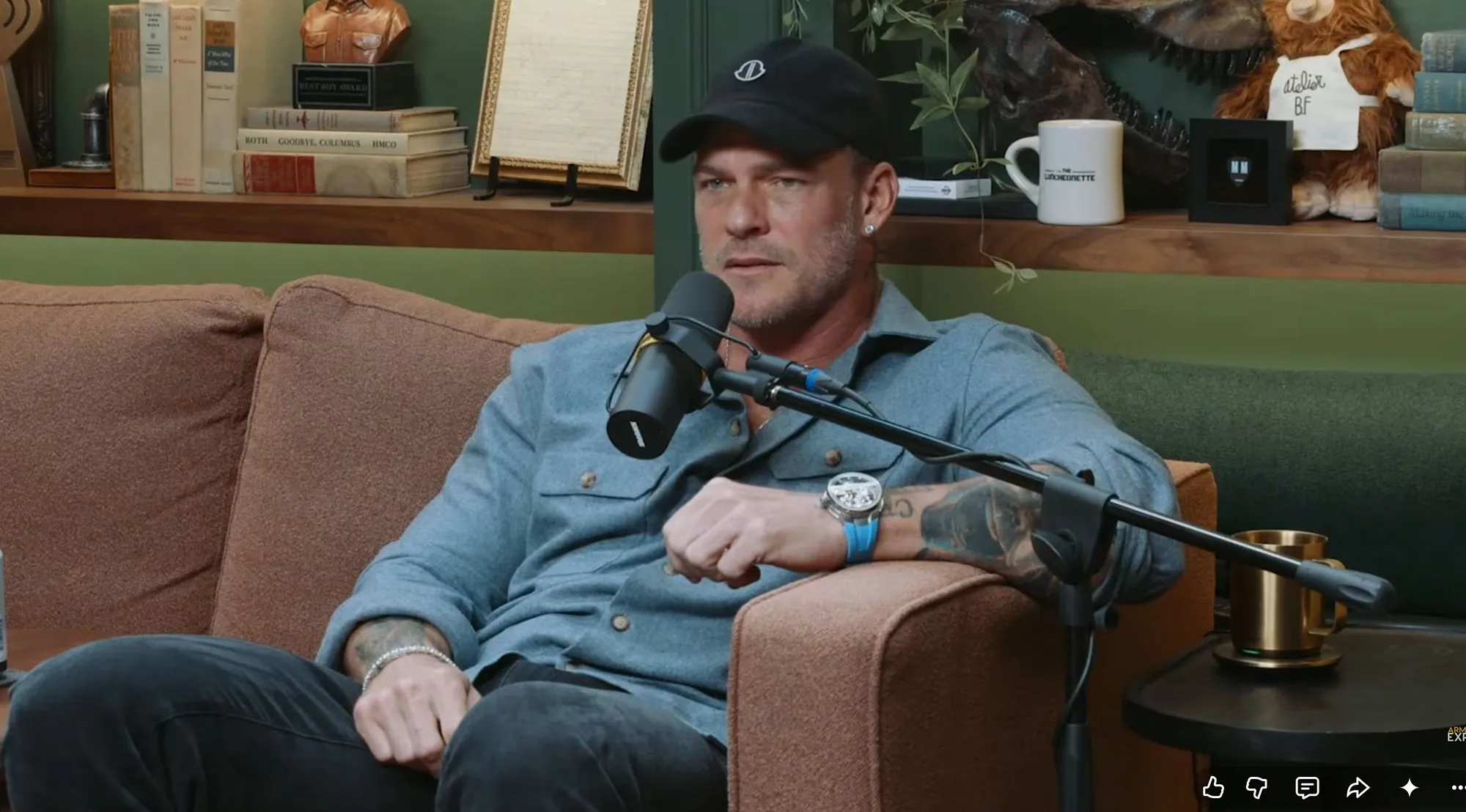 Alan Ritchson sitting on a couch with a microphone in front of him.