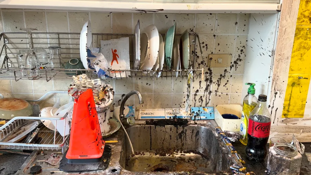 A kitchen sink and surrounding countertop covered in black splattered paint.