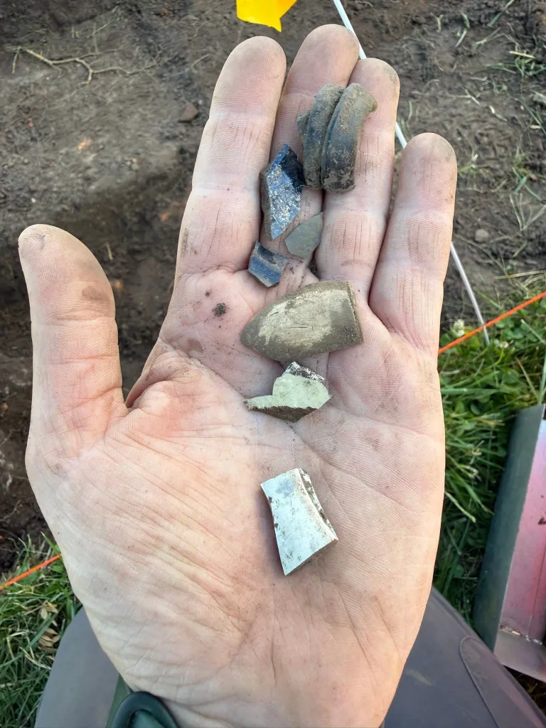 A hand holds various pieces of pottery shards found during an archaeological excavation.
