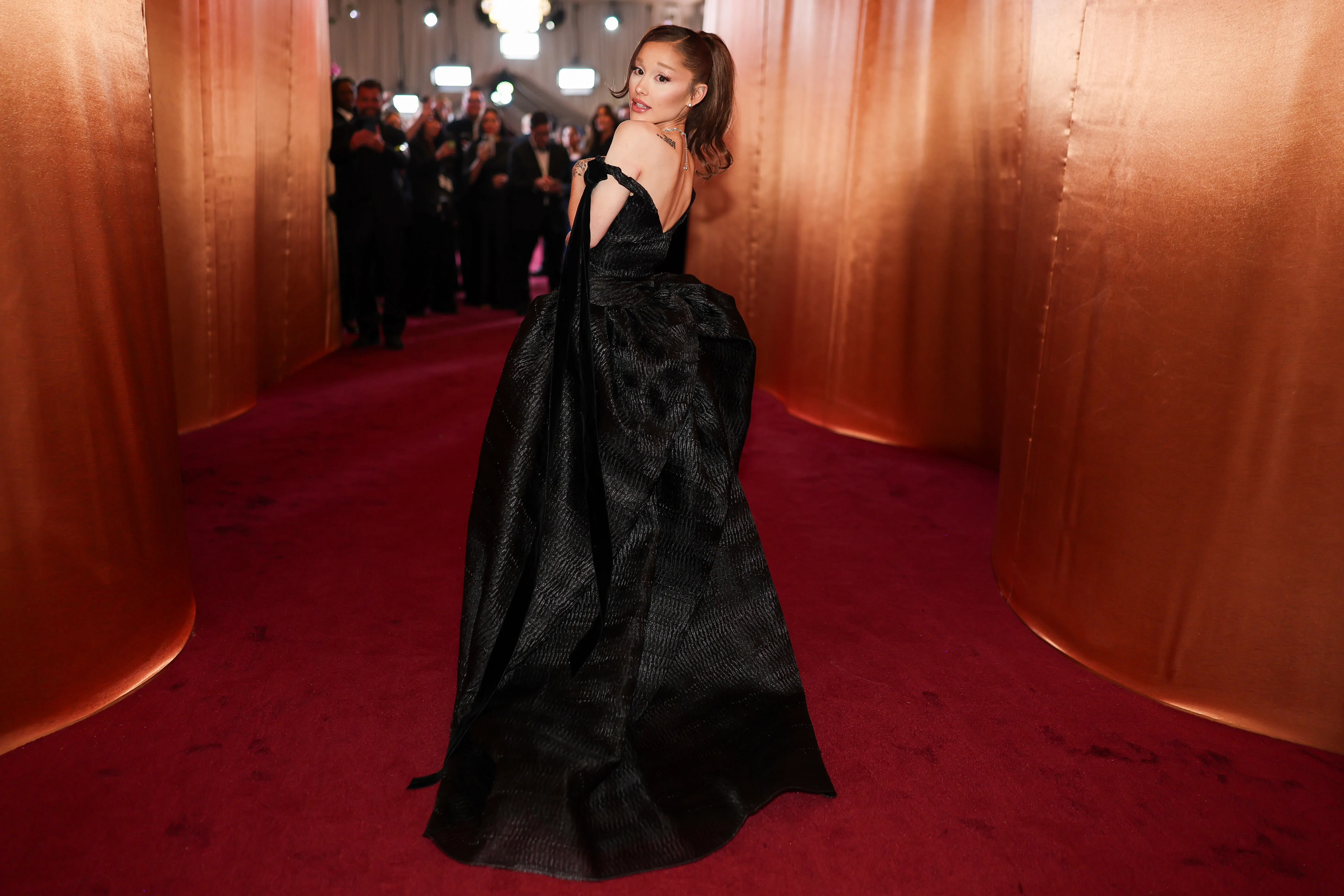 Ariana Grande poses on the red carpet in a black, off-the-shoulder gown.