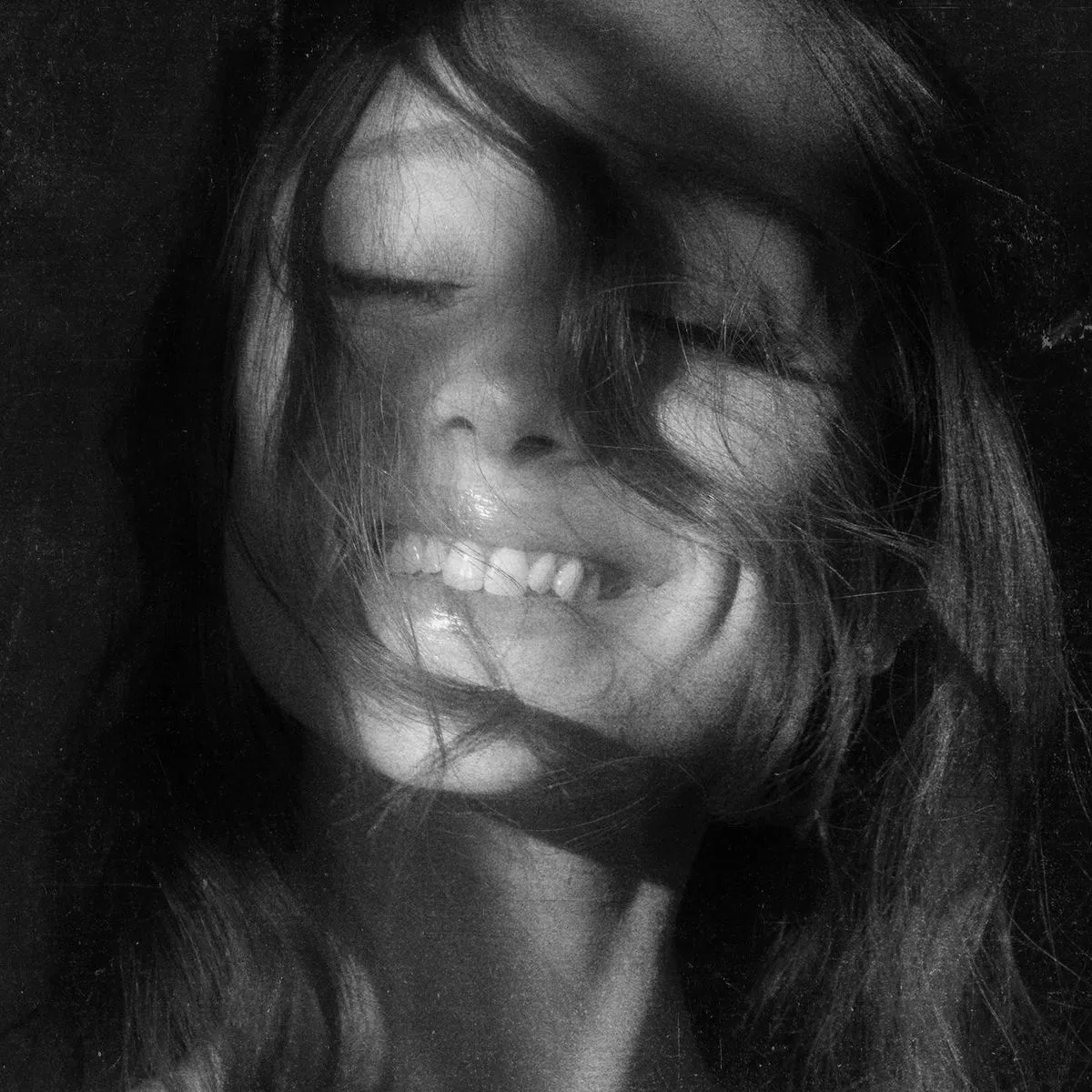 Black and white close-up of a smiling person with eyes closed and hair covering parts of their face.