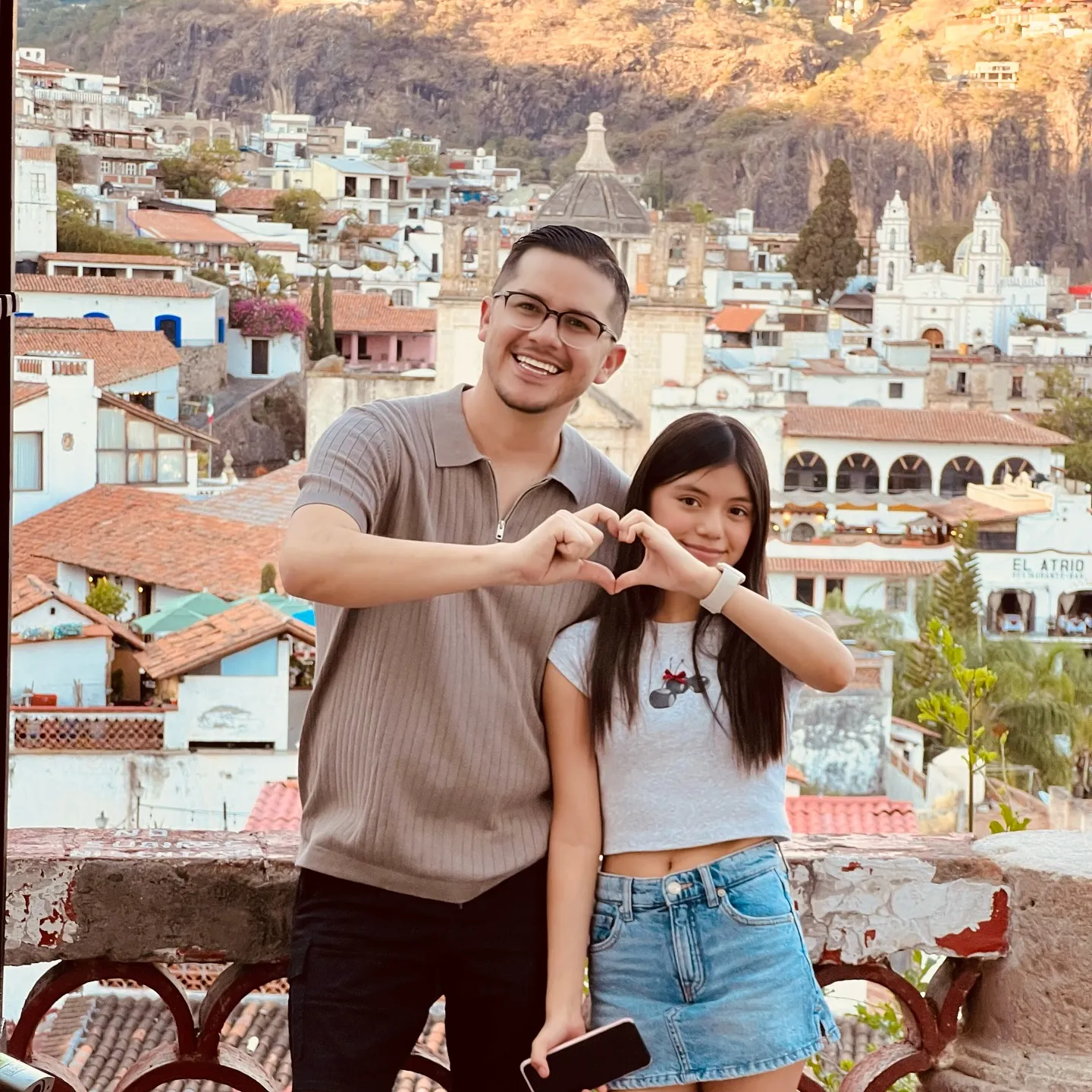 Armando and Hannah Rubio forming a heart shape with their hands in a scenic town.