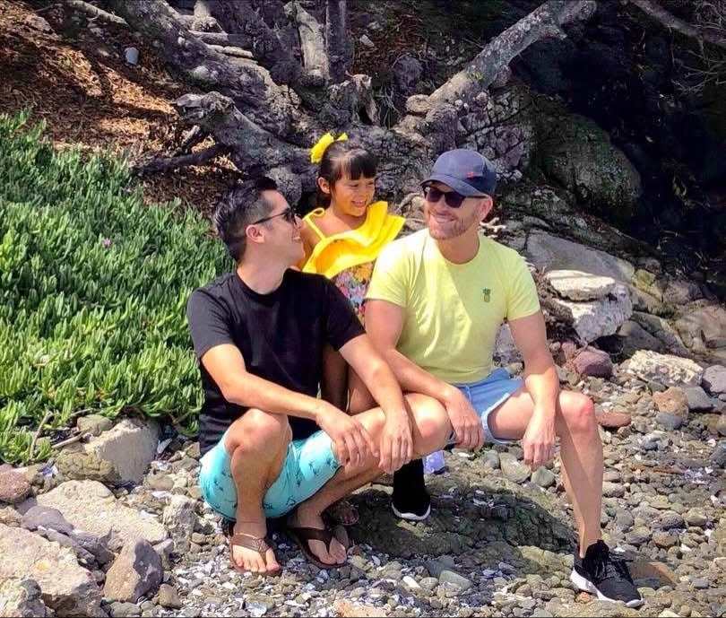 Armando Niedermeier-Rubio, his partner, and daughter smiling while squatting outdoors.