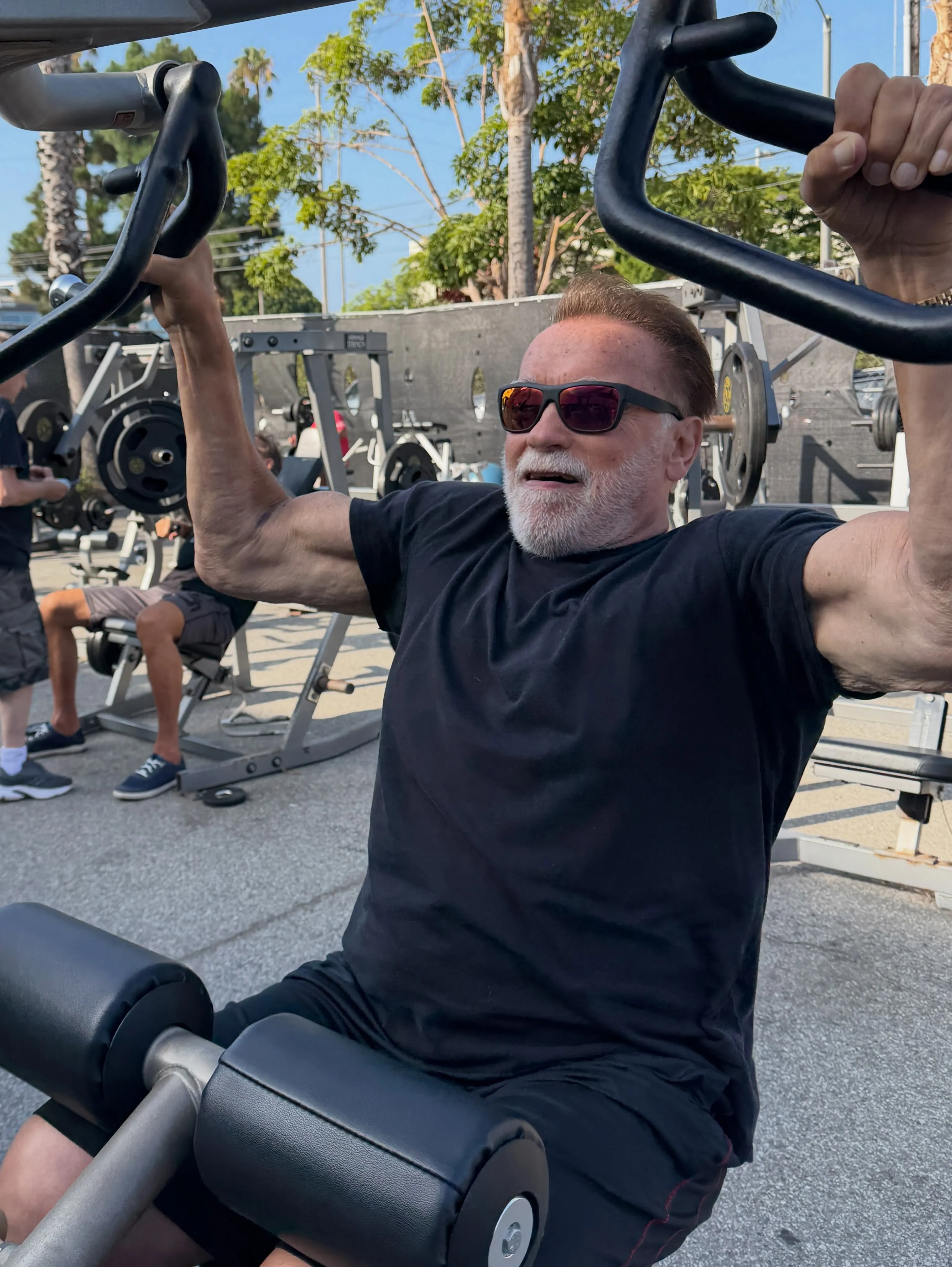 Arnold Schwarzenegger lifts weights outdoors, celebrating his 79th birthday.