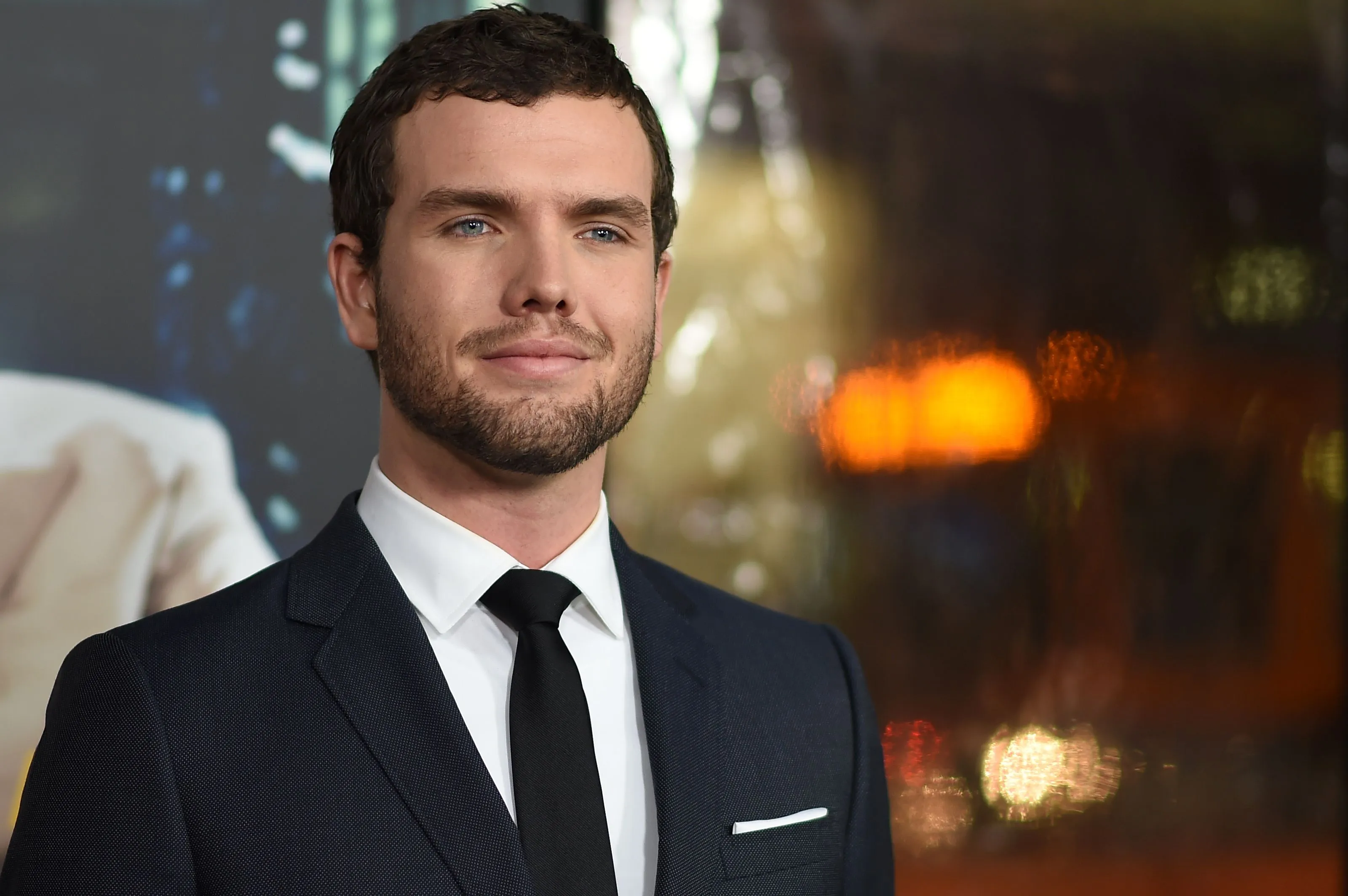 Austin Swift in a suit and tie, smiling faintly at the premiere of 