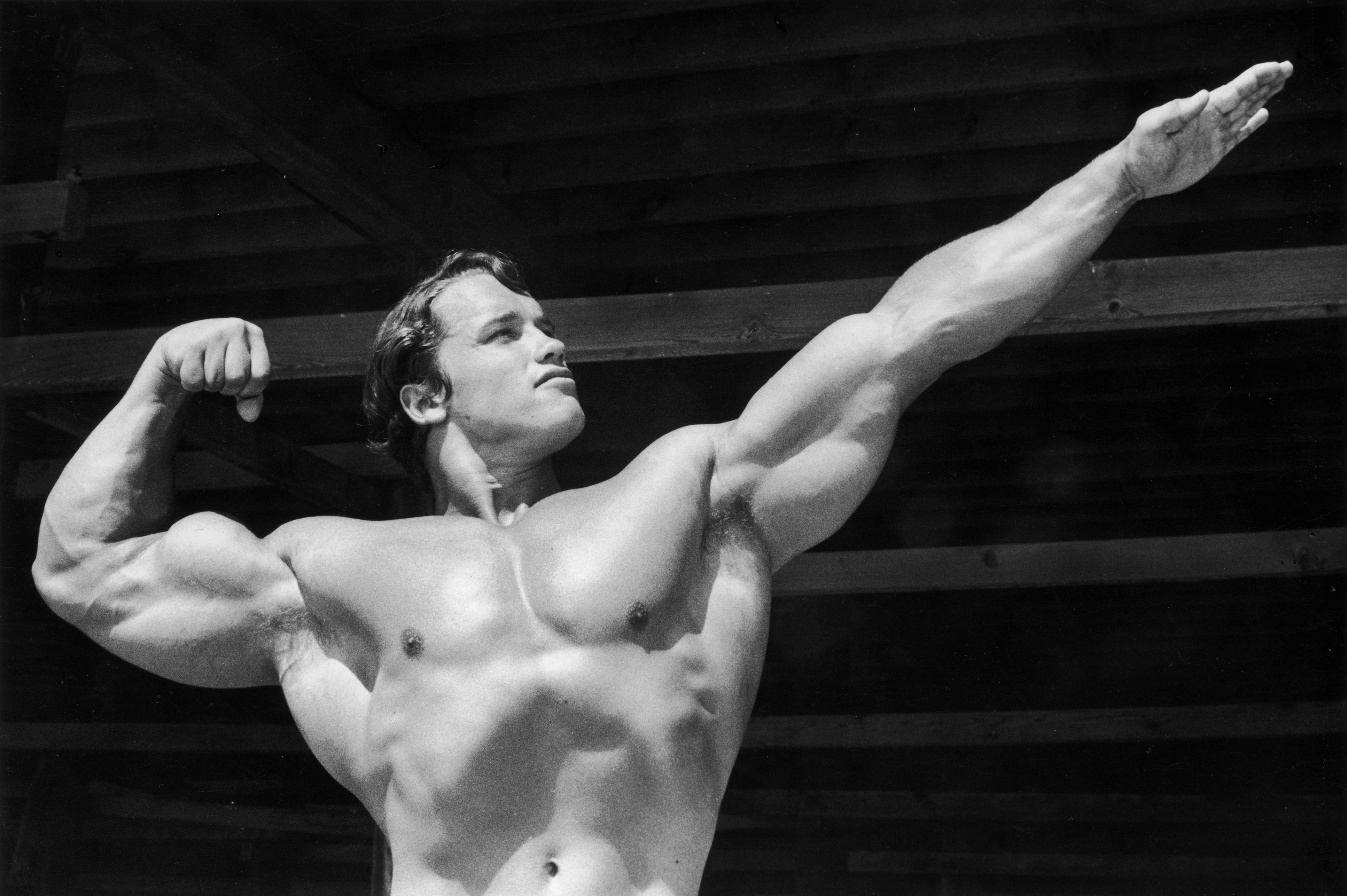 Arnold Schwarzenegger flexing on Muscle Beach in black and white.