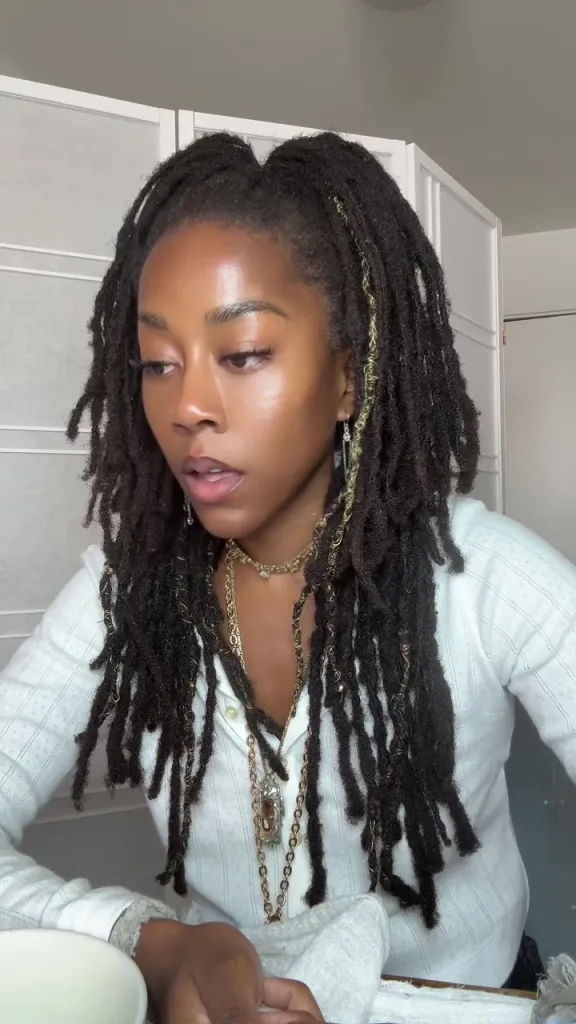 A woman with long dreadlocks and gold jewelry looking down.