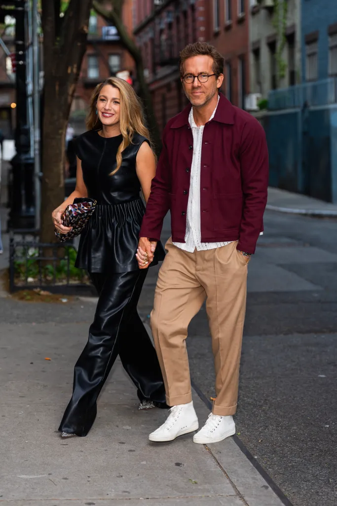Blake Lively and Ryan Reynolds holding hands and smiling while walking outdoors.