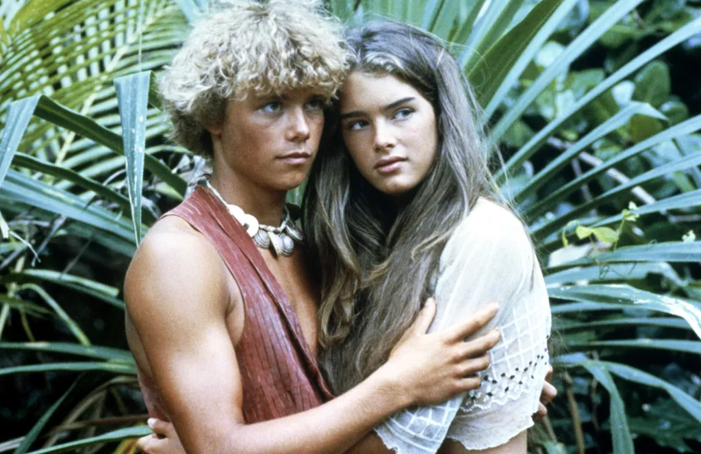 Christopher Atkins and Brooke Shields in an embrace, framed by tropical foliage, in 