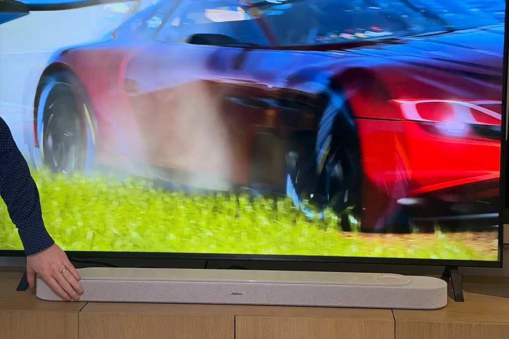 A Bose soundbar in front of a TV displaying a race car.