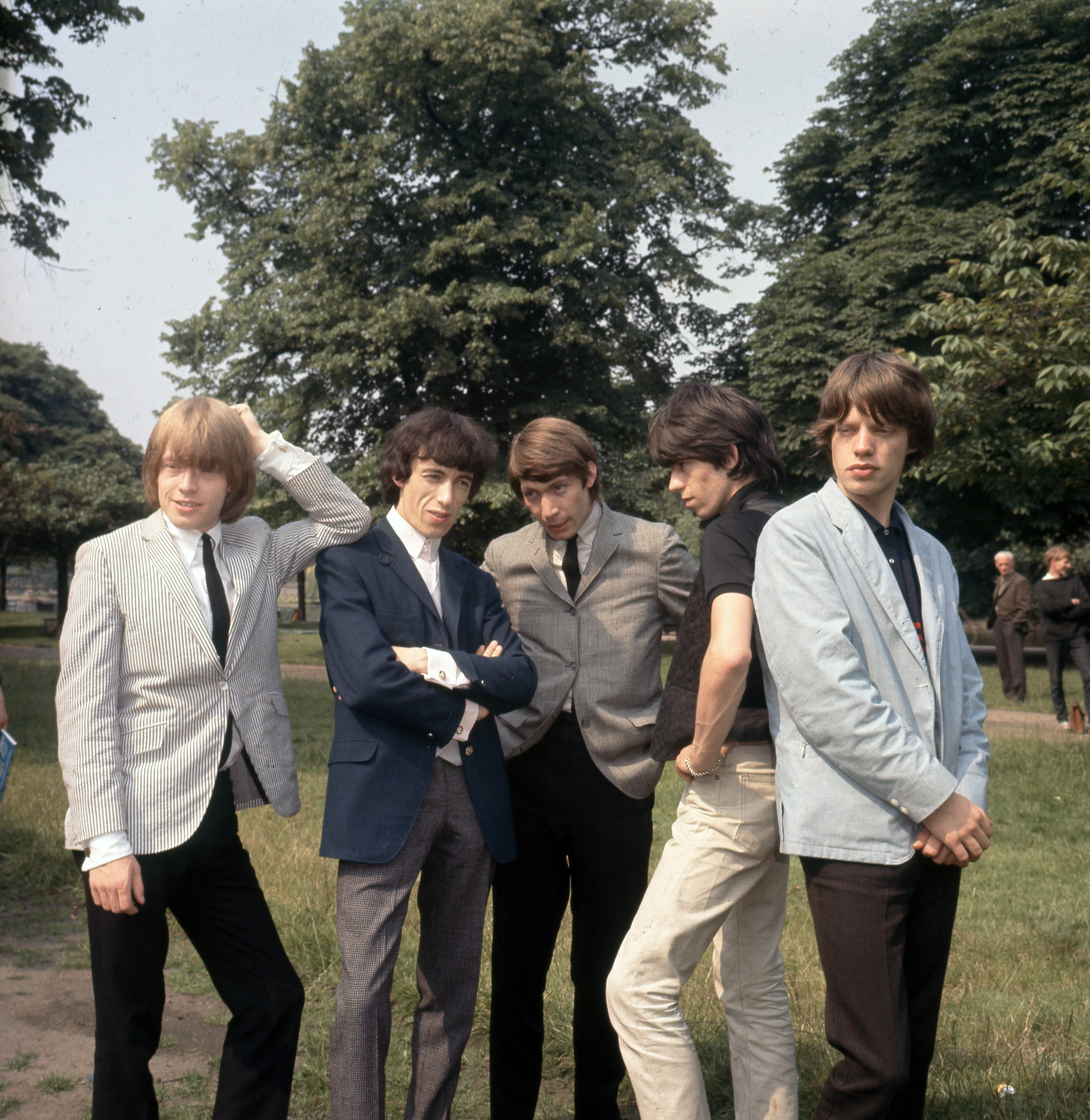 The Rolling Stones members Brian Jones, Bill Wyman, Charlie Watts, Keith Richards, and Mick Jagger pose for a group photo outdoors.