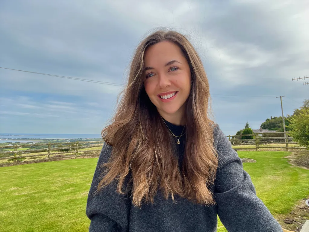 Laura Murphy, smiling in a grey sweater with a landscape in the background.