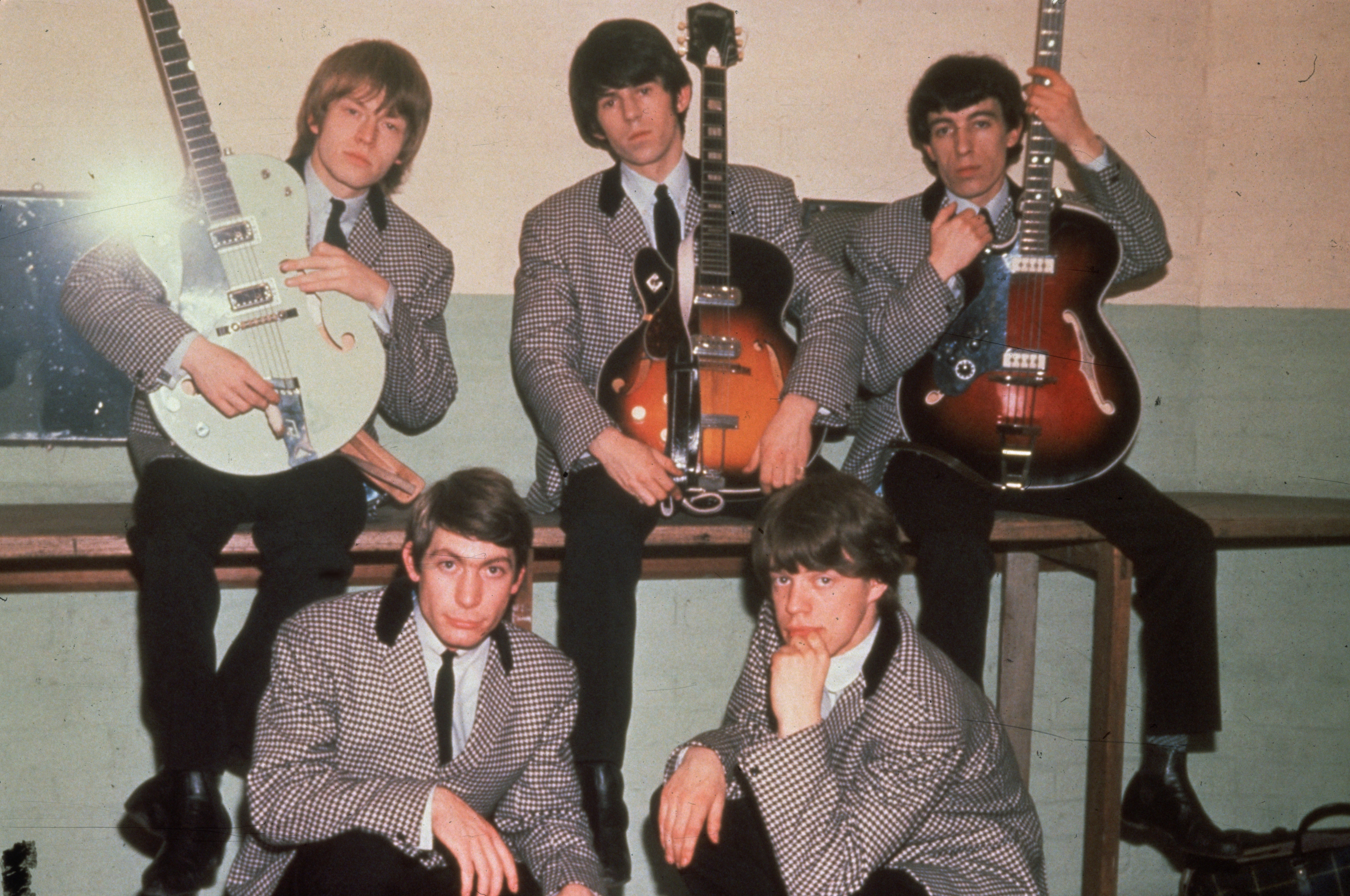 The Rolling Stones rock group in 1964, with Charlie Watts and Mick Jagger in front, and Brian Jones, Keith Richards, and Bill Wyman behind them holding guitars.