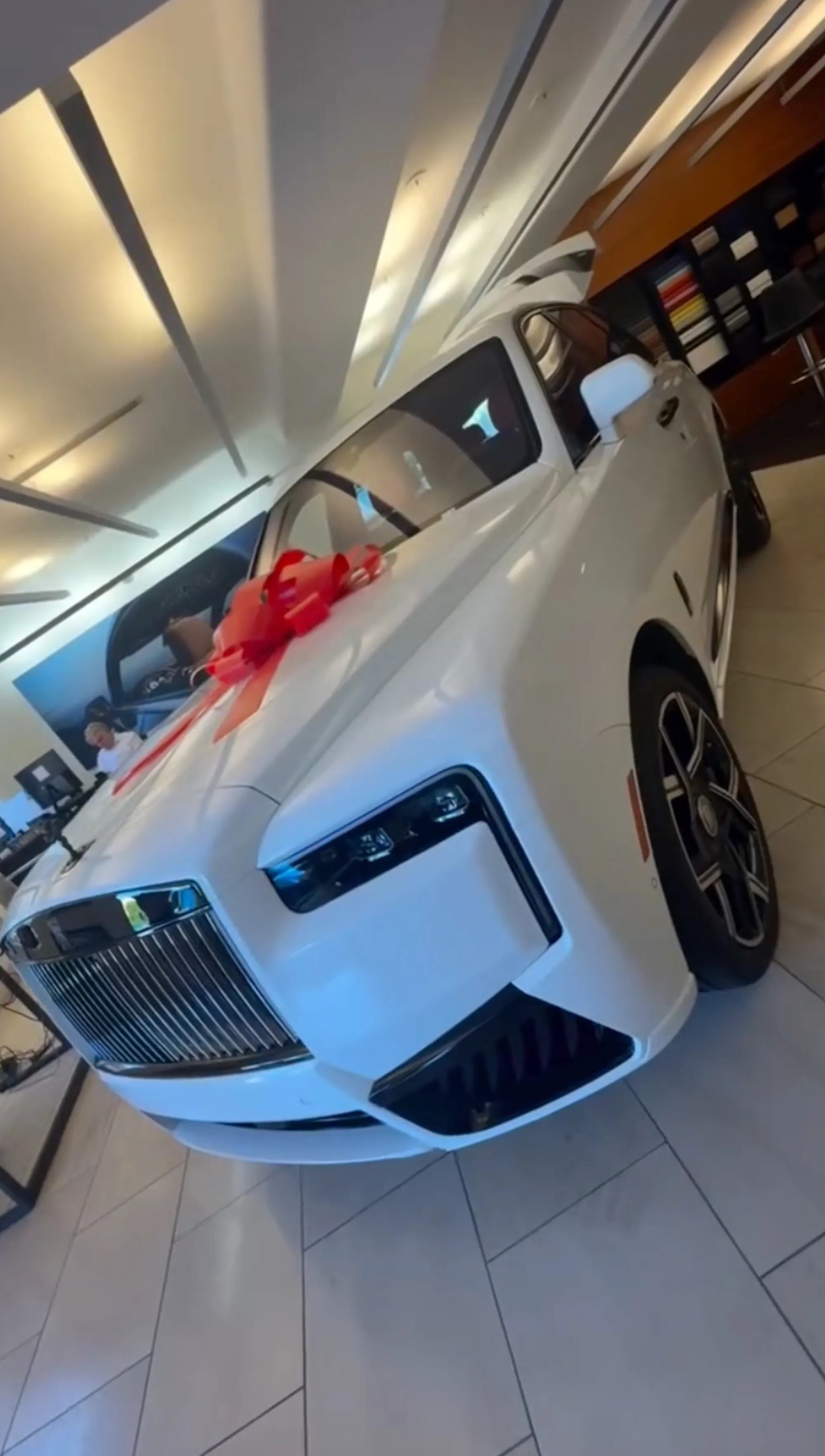 A white Rolls-Royce with a large red bow on the hood.
