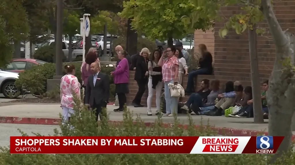 Shoppers stand and sit outside a mall after an evacuation, with a news chyron at the bottom reporting 