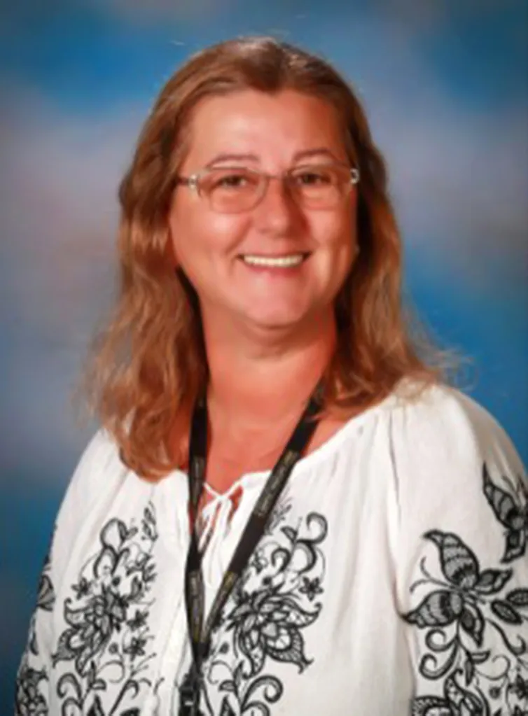 Portrait of Cristina Irimie, a woman with long light brown hair and glasses, wearing a white shirt with black floral embroidery.
