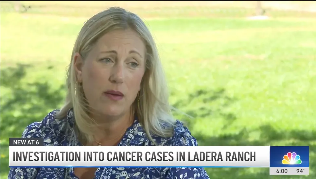 A blonde woman in a blue patterned shirt is interviewed outdoors, with text overlay