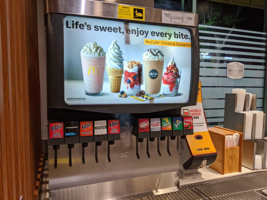 A Coca-Cola soda fountain with Fanta, Powerade, Water, Dr. Pepper, Sprite, and an ad for McCafe Drinks and Desserts.