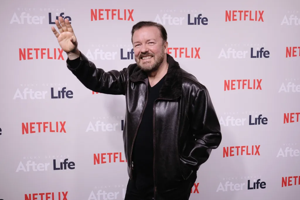 Comedian Ricky Gervais waves and smiles at the