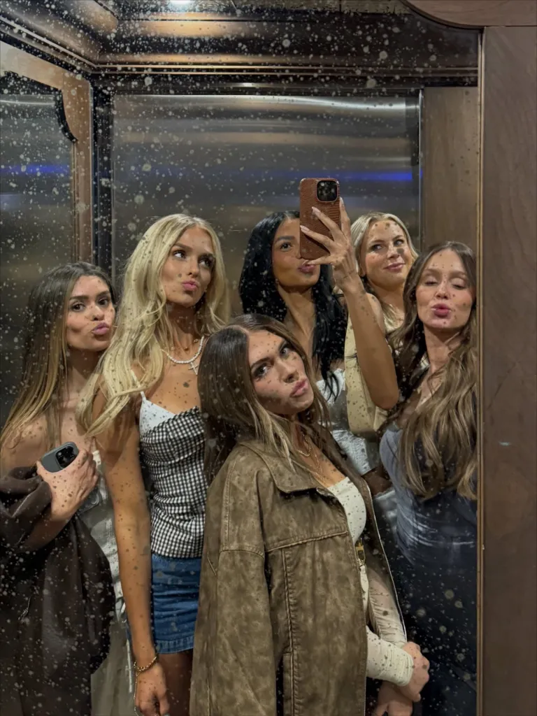 Six young women posing in a dirty mirror for a selfie.