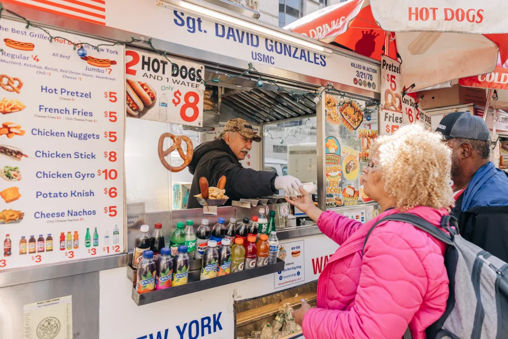 Dan Rossi, the Hot Dog King, serving a hot dog to a customer from his food cart in Manhattan.