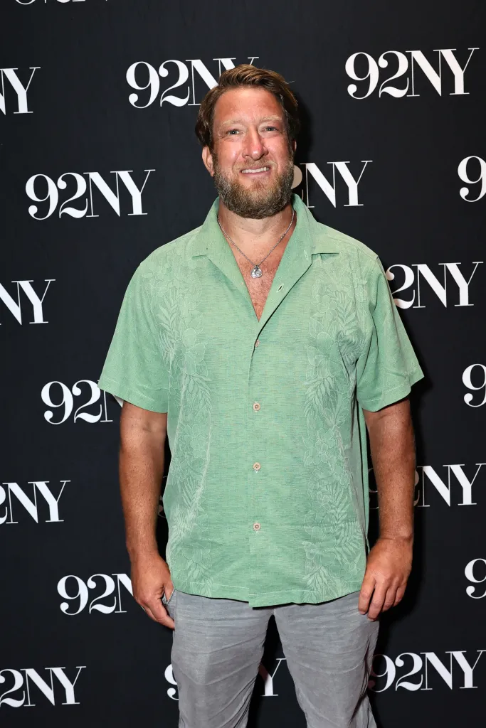 Dave Portnoy, with a beard and light green shirt, standing in front of a black background with