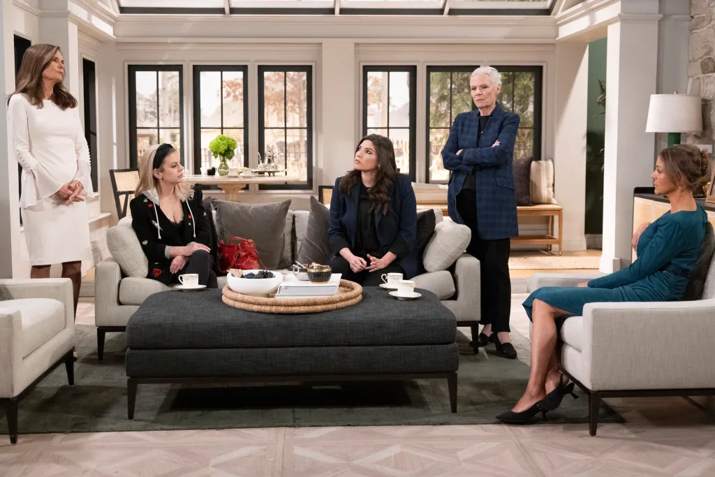 Five women in a living room, some seated, some standing, in a dramatic scene from 