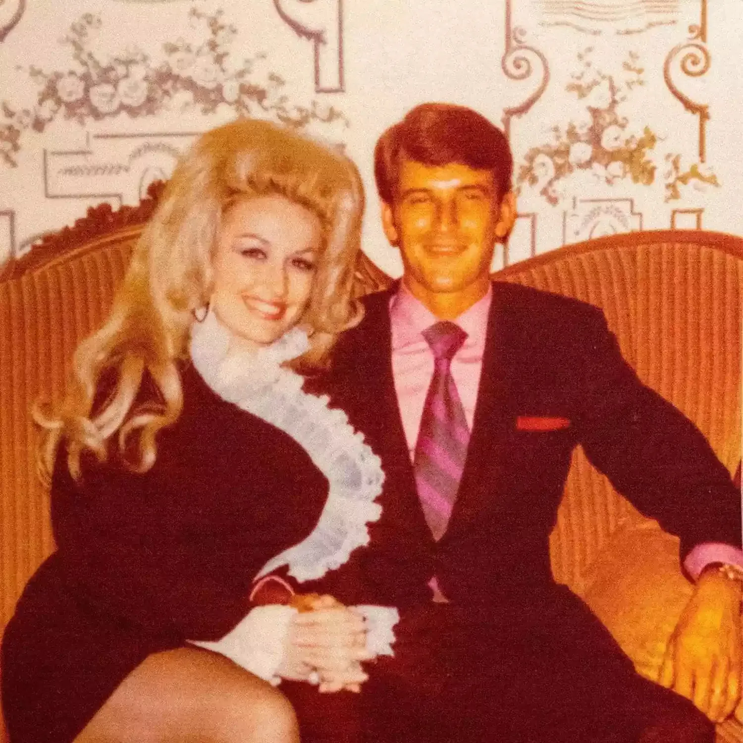 Dolly Parton and her husband Carl Thomas Dean smiling on a couch.