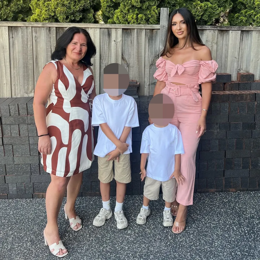 Donike Gocaj, wearing a white and brown dress, posing with two children and a woman in a pink outfit.