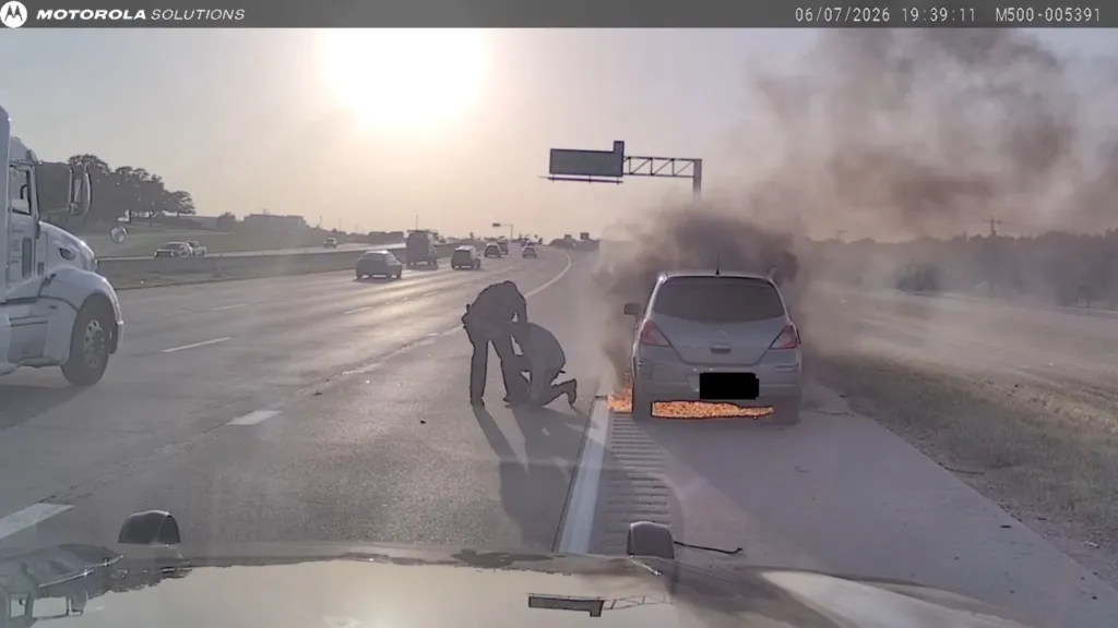 Two people on a highway assisting a third person next to a smoking car.