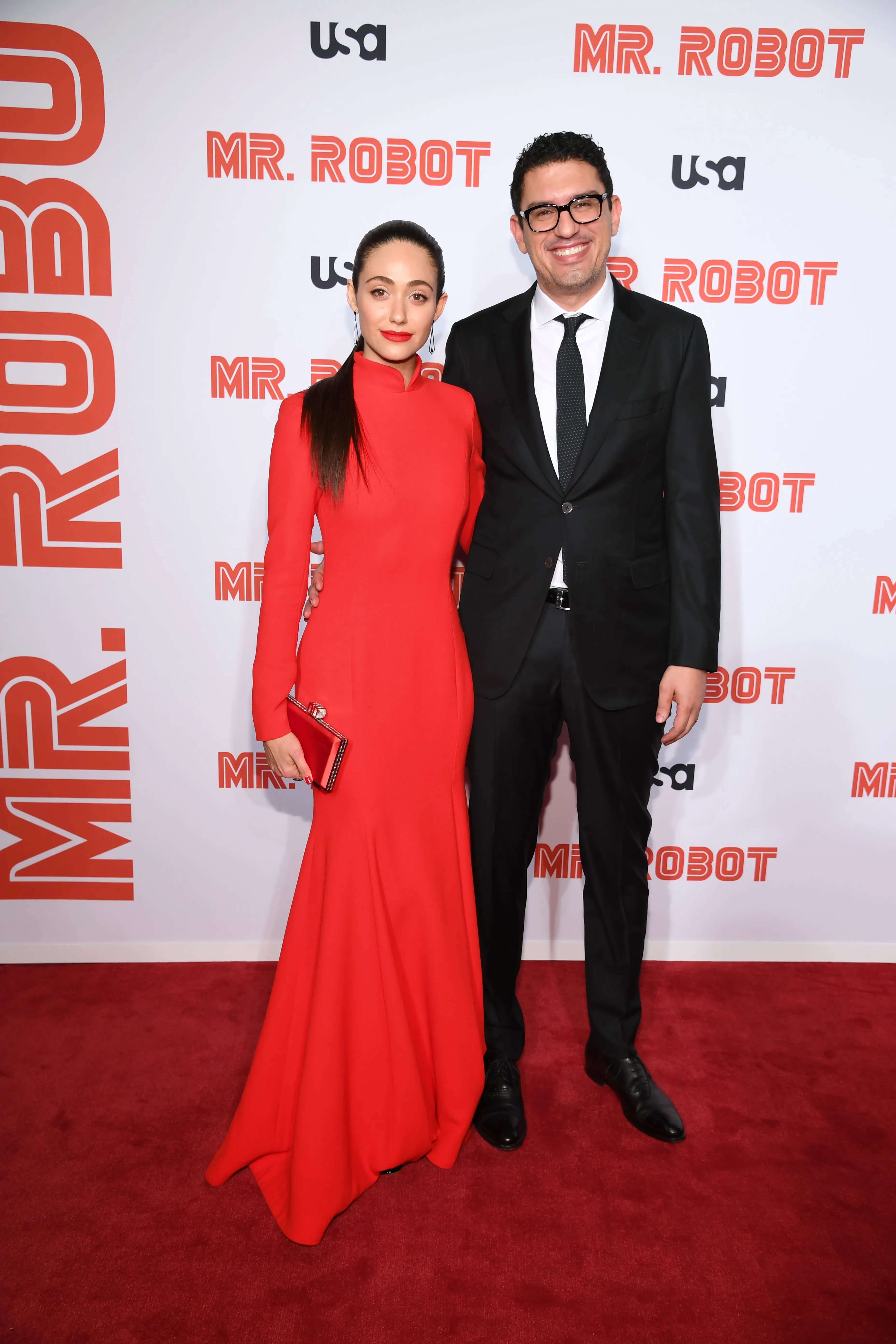 Emmy Rossum in a red gown and Sam Esmail in a suit on the red carpet for the 