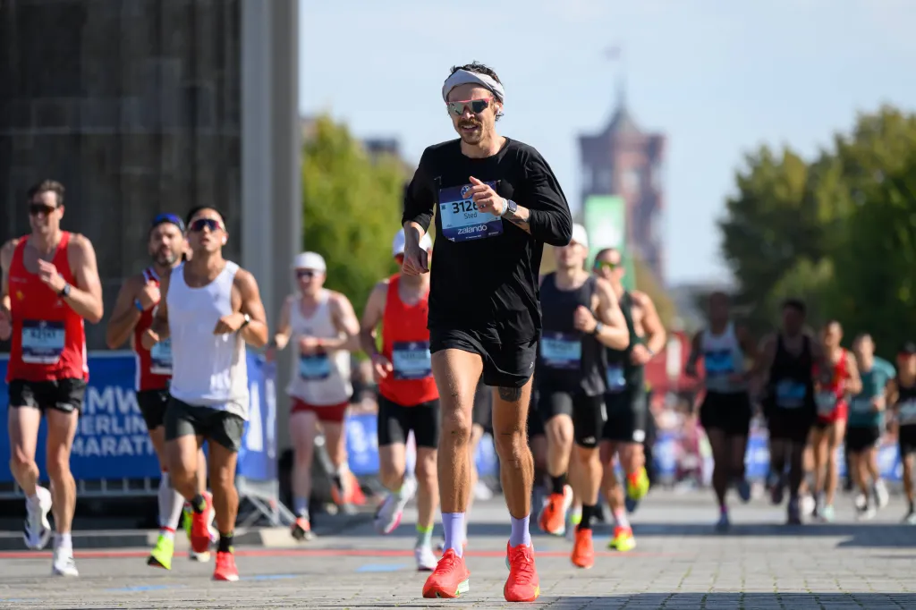 Harry Styles, wearing black top, black shorts, pink sneakers and sunglasses and a headband, running in the BMW Berlin Marathon.