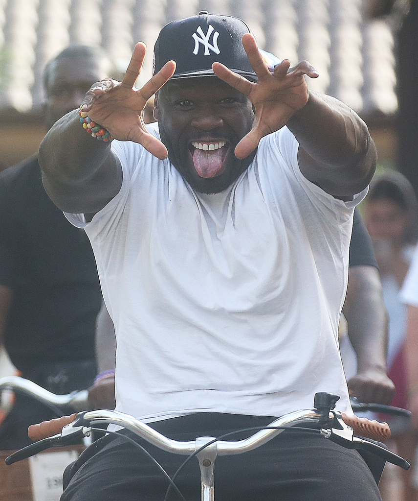 Rapper 50 Cent on a bike, sticking out his tongue and making a hand gesture with both hands.
