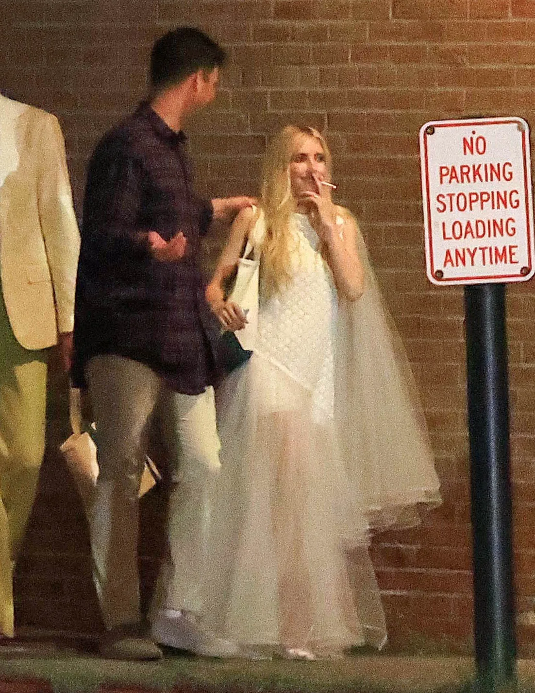 Emma Roberts in a white dress, smoking a cigarette, next to a man and a 