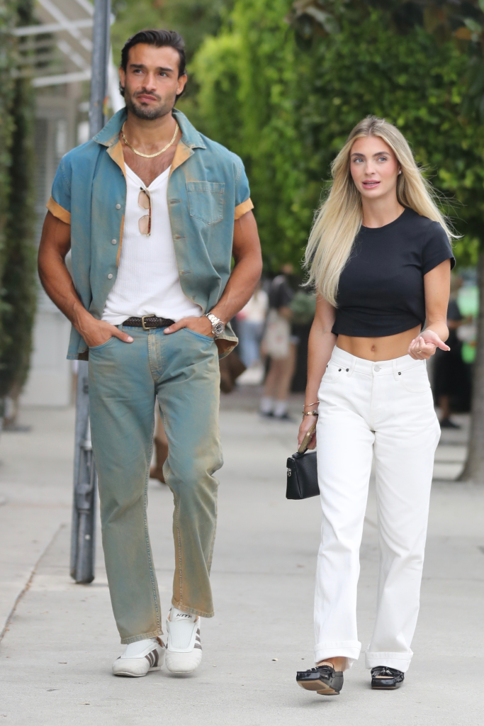 Sam Asghari, in a blue shirt, white T-shirt, bue jeans, and Brooke Irvine, in a black cropped T-shirt and white jeans, walking at a farmers market.