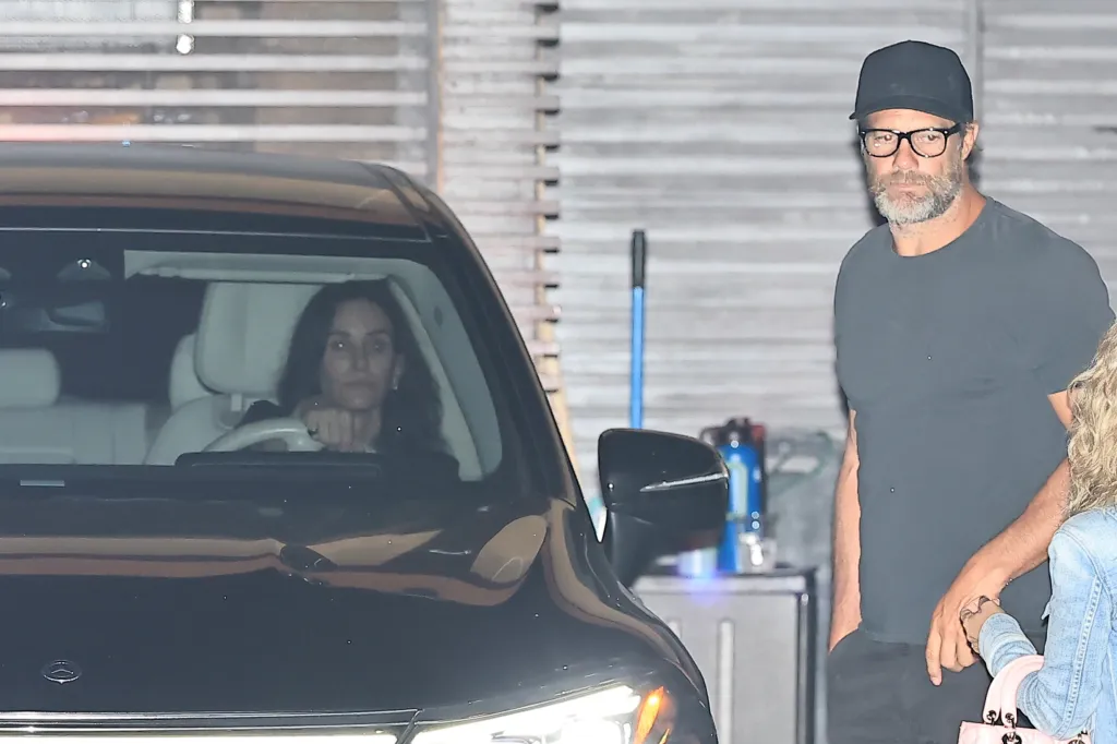 Courteney Cox in a car and Geoff Stults next to the car.