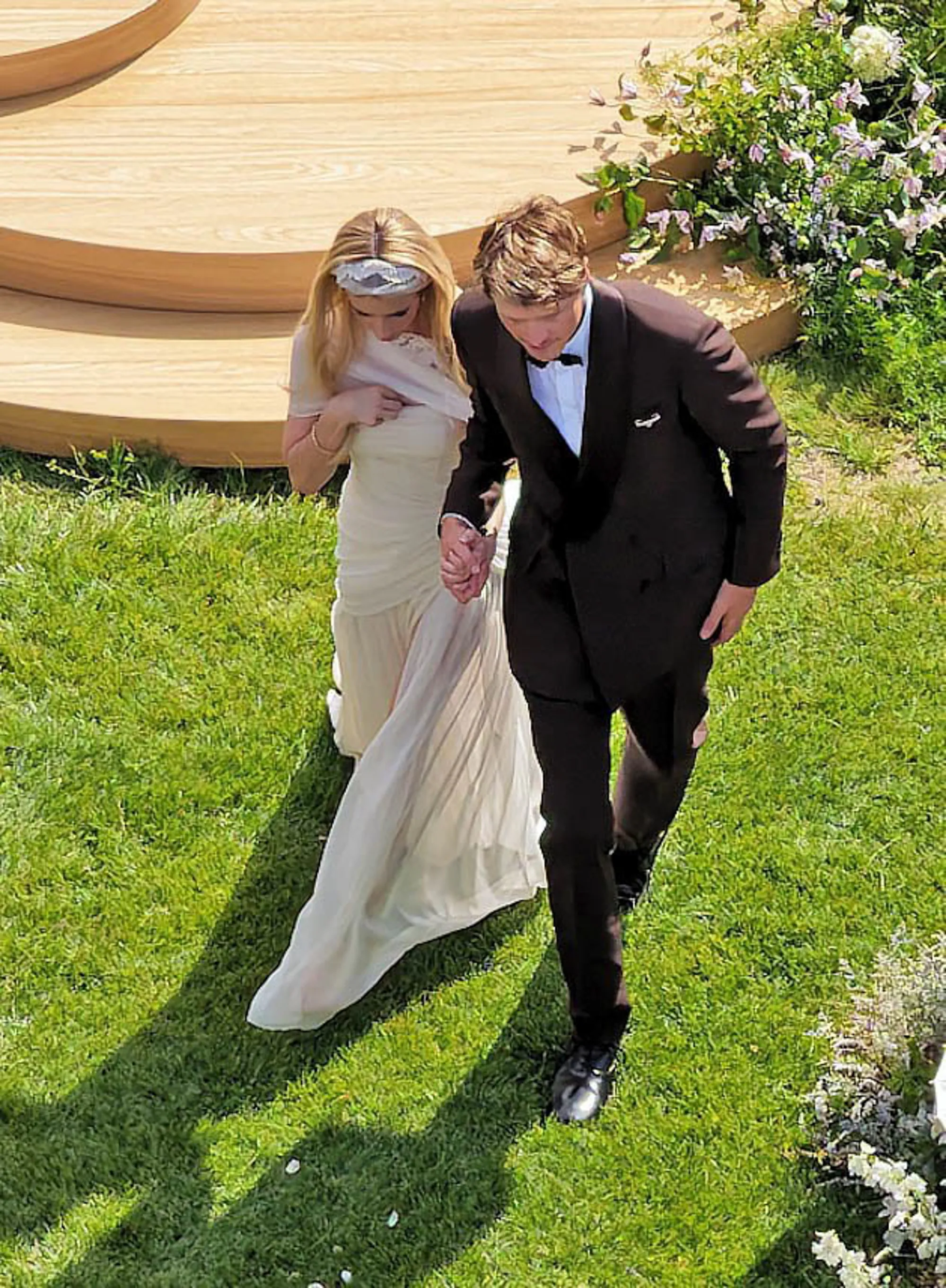 Emma Roberts in a white dress and Cody John in a brown suit walking hand in hand.